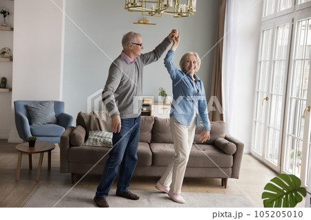Happy senior couple holding hands dancing in living room Happy senior couple holding hands dancing in living room 105205010