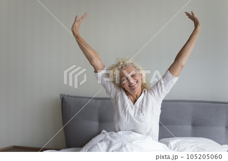 Cheerful blonde mature woman awaking in fresh white linen Cheerful blonde mature woman awaking in fresh white linen 105205060