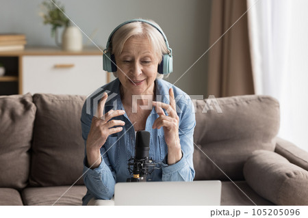 Elderly female blogger wear headphones speaking into professional microphone Elderly female blogger wear headphones speaking into professional microphone 105205096