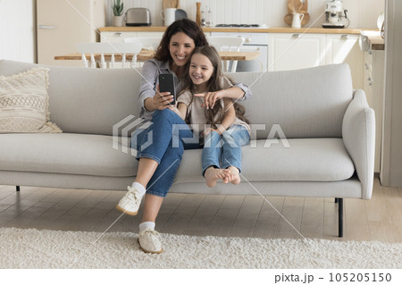 Cheerful pretty mother hugging sweet happy kid girl, using smartphone Cheerful pretty mother hugging sweet happy kid girl, using smartphone 105205150
