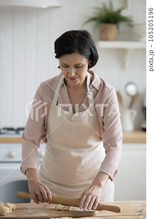 Positive mature home baker woman in cooking apron preparing pastry Positive mature home baker woman in cooking apron preparing pastry 105205196