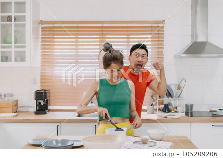 Lover couple. Funny shocked face reaction of husband looking at wife cooking. Lover couple. Funny shocked face reaction of husband looking at wife cooking. 105209206