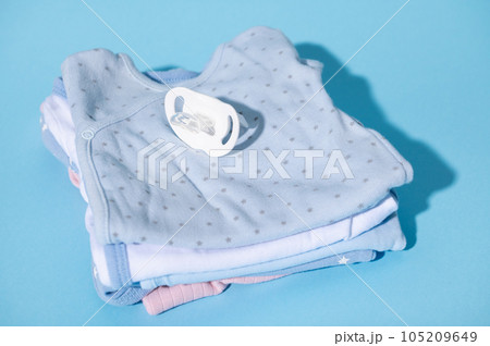 Still life with a baby comforter and clean baby clothes prepared for the birth of child, isolated over blue background Still life with a baby comforter and clean baby clothes prepared for the birth of child, isolated over blue background 105209649