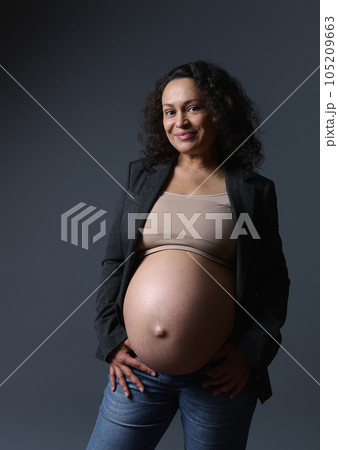 Bbeautiful young adult pregnant woman with big belly in pregnancy trimester third, smiling at camera, isolated on gray Bbeautiful young adult pregnant woman with big belly in pregnancy trimester third, smiling at camera, isolated on gray 105209663