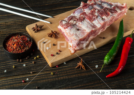 Fresh meat ribs on a kitchen cutting board with seasonings and hot peppers. Cooking a delicious grilled lunch at home Fresh meat ribs on a kitchen cutting board with seasonings and hot peppers. Cooking a delicious grilled lunch at home 105214424