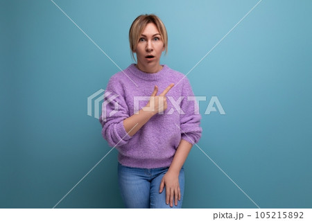 portrait of a shocked surprised blond young woman in a casual look shows her hand to the side on a 105215892