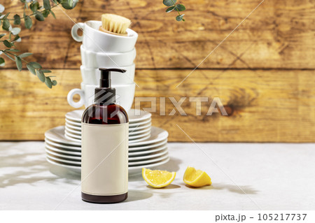 Mockup of dish detergent. Eco friendly natural cleaning dishes. Bottle with dish detergent with clean plates and cups on wooden background with sprig of eucalyptus. Front view, copy space 105217737