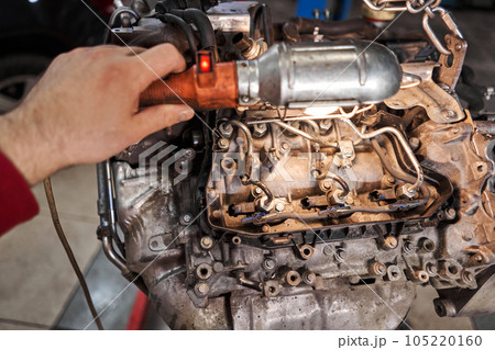 A car mechanic inspects the engine with a flashlight. Engine Block on a repair stand with Special crane jack. Technical service station for car. 105220160