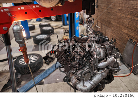 A car mechanic inspects the engine with a flashlight. Engine Block on a repair stand with Special crane jack. Technical service station for car. 105220166