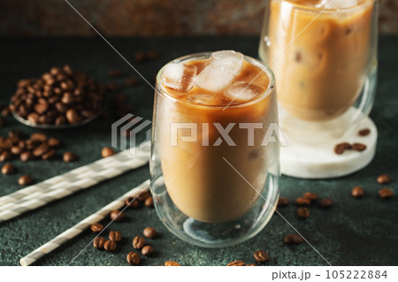 Ice coffee in a tall glass with cream poured over, ice cubes and beans on a dark concrete table. Ice coffee in a tall glass with cream poured over, ice cubes and beans on a dark concrete table. 105222884
