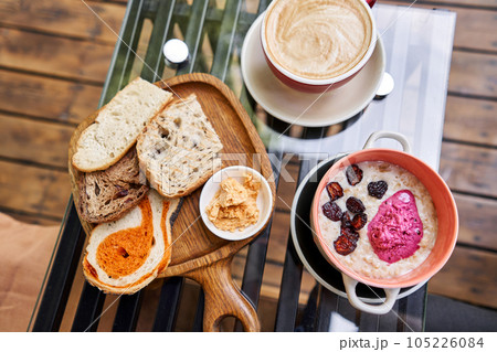 Breakfast with fresh cooked porridge served with Dry Cherry with strawberry sorbet in bowl. Assorted sliced bread on a wooden board. Served with smoked butter. Breakfast with cappuccino coffee. 105226084