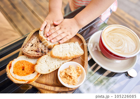 Little girl eats sliced bread. Composition with butter and bread on wooden plate. Breakfast at the bakery cafe. Little girl eats sliced bread. Composition with butter and bread on wooden plate. Breakfast at the bakery cafe. 105226085