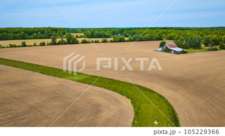 Aerial flat farmland with barren fields and patch of green grass snaking through desert area 105229366