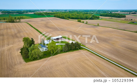 Aerial clean farmhouse landscape property aerial with green runoff ditches, paved road, empty fields 105229394