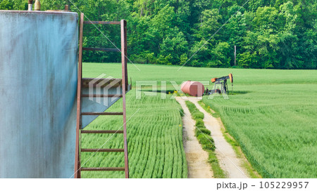 Metal steps and oil pump jack in middle of grass field with maintenance road 105229957