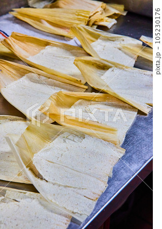 Vertical of silver tray of several pre-baked tamales with masa and corn husk exposed 105230176