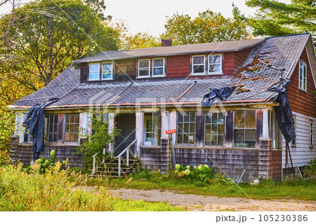 Red shingles falling off old abandoned house with black tarp broken shingles and wood steps 105230386