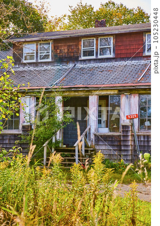 Abandoned urban home with broken missing roof shingles red and black walls overgrowth Abandoned urban home with broken missing roof shingles red and black walls overgrowth 105230448
