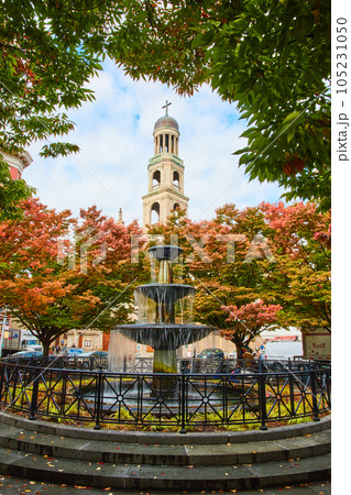Stunning fountain surrounded by fall leaves in city with Christian Church steeple behind in New York City 105231050