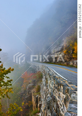 Foggy morning on road through cliffs next to stone block wall 105231162