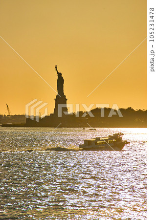 Silhouette of Statue of Liberty in soft golden light with ship sailing past in foreground over glistening waters Silhouette of Statue of Liberty in soft golden light with ship sailing past in foreground over glistening waters 105231478