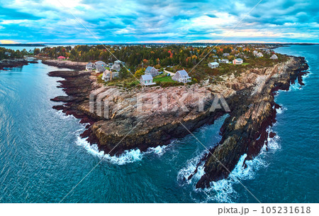 Stunning aerial over rocky coasts of Maine on the ocean with houses, fall foliage, and dusk light 105231618