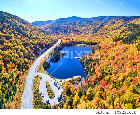 Wide aerial panorama of blue lake and peak fall foliage mountains of New Hampshire along road with tourist overlook 105231619