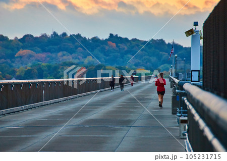 Joggers running along long cement bridge boardwalk with forests in background 105231715