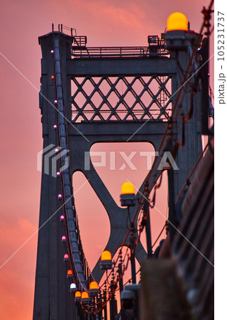 Orange lights in detail on support wires of American bridge with golden light behind 105231737