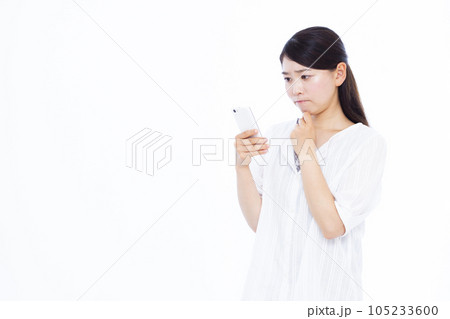 白い背景の前でスマホを持ち悩んでいる30代の女性 白い背景の前でスマホを持ち悩んでいる30代の女性 105233600
