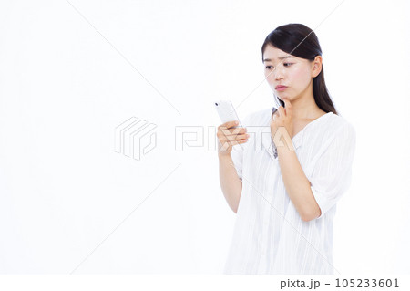 白い背景の前でスマホを持ち悩んでいる30代の女性 白い背景の前でスマホを持ち悩んでいる30代の女性 105233601
