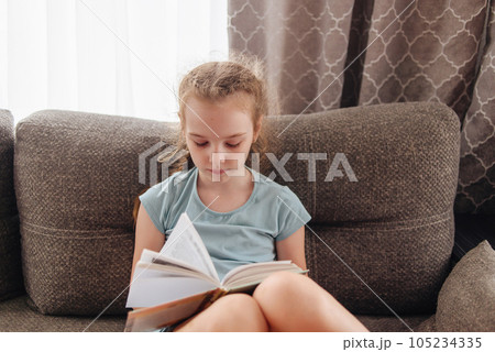 Girl reading a book for school program sitting on the couch. The theme of books and reading. High quality photo 105234335