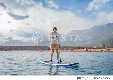 Young men Having Fun Stand Up Paddling in blue water sea near st stefan island in Montenegro. SUP Young men Having Fun Stand Up Paddling in blue water sea near st stefan island in Montenegro. SUP 105237595