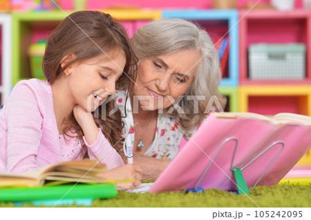 portrait of granddaughter with grandmother doing homework and reading books 105242095