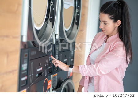 Young woman pressing button in washing machine at public laundry. 105247752