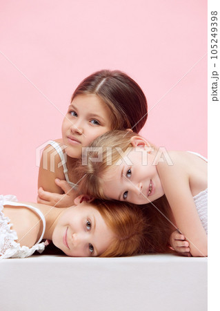 Portrait of little beautiful children, girls posing together against pink studio background. Well-being 105249398