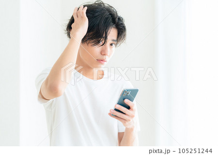 リビングの窓際でスマホを操作しながらヘアケアをする若い男性 リビングの窓際でスマホを操作しながらヘアケアをする若い男性 105251244