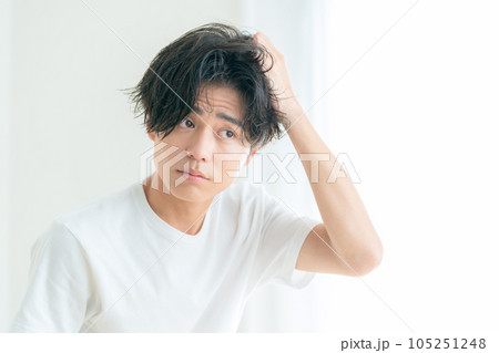 リビングの窓際でヘアケアをする若い男性 105251248