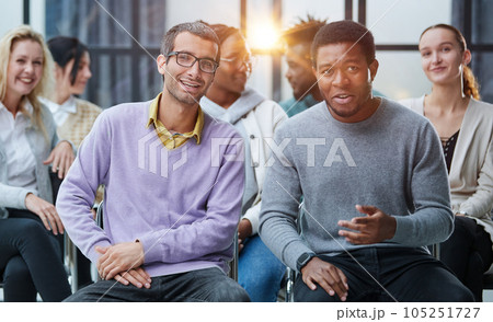 Young people enjoying spending time together on special group therapy. Handsome joyful guy talking jokes and making fun. 105251727