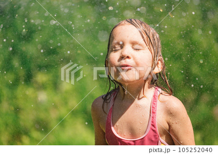 Happy child refreshing with garden sprinkler  on a hot summer day 105252040