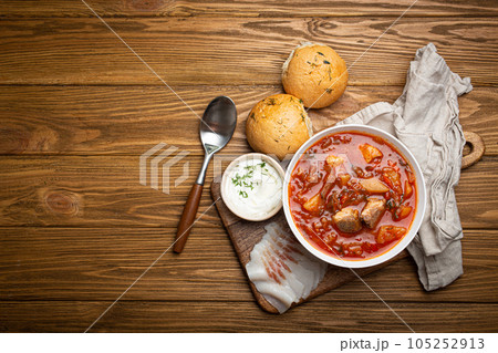 Ukrainian Borscht, red beetroot soup with meat, in white bowl with sour cream, garlic buns Pampushka and salo slices, rustic stone background. Traditional authentic dish of Ukraine, space for text Ukrainian Borscht, red beetroot soup with meat, in white bowl with sour cream, garlic buns Pampushka and salo slices, rustic stone background. Traditional authentic dish of Ukraine, space for text 105252913