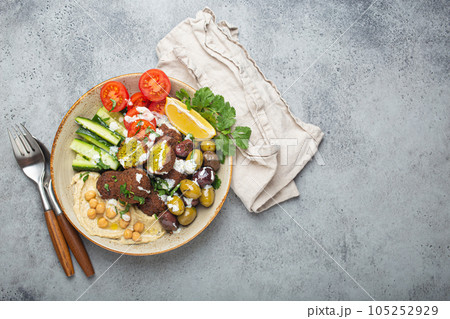 Falafel salad bowl with hummus, vegetables, olives, herbs and yogurt sauce. Vegan lunch plate top view on rustic stone background, healthy meal with falafel and veggies, copy space Falafel salad bowl with hummus, vegetables, olives, herbs and yogurt sauce. Vegan lunch plate top view on rustic stone background, healthy meal with falafel and veggies, copy space 105252929