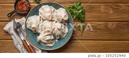 Georgian dumplings Khinkali on plate with red tomato sauce and fresh cilantro top view, rustic wooden background, traditional dish of Georgia, space for text Georgian dumplings Khinkali on plate with red tomato sauce and fresh cilantro top view, rustic wooden background, traditional dish of Georgia, space for text 105252940