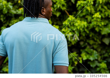 Rear view of african american man with dreadlocks wearing pale blue polo shirt in garden, copy space 105254566