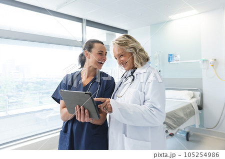 Happy caucasian female doctors with stethoscopes using tablet at hospital Happy caucasian female doctors with stethoscopes using tablet at hospital 105254986