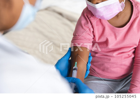 African american female doctor wearing face mask vaccinating girl patient at hospital 105255045