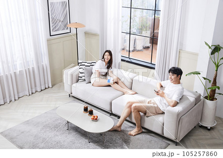 summer lifestyle, korean asian young couple sitting on couch and watching television summer lifestyle, korean asian young couple sitting on couch and watching television 105257860