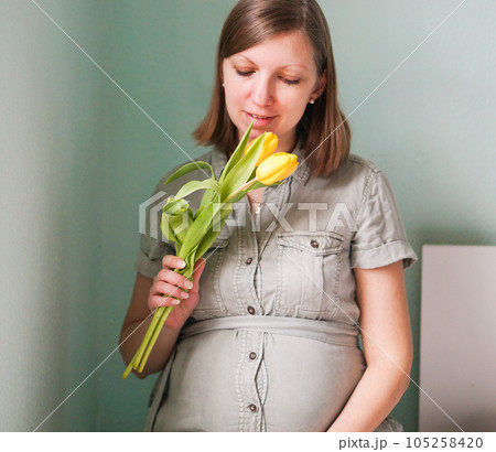 Attractive smiling pregnant woman in dress with yellow flowers at home. Attractive smiling pregnant woman in dress with yellow flowers at home. 105258420