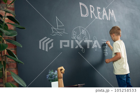 Little boy, child standing at black and drawing his dreamings about being musician. Imagination. Psychology and creative thinking 105258533