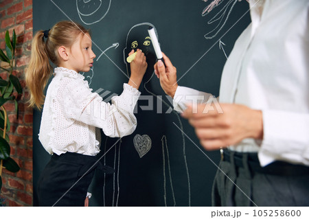 Little girl, child, student of primary school learning anatomy with teacher in classroom. Drawing human shape on blackboard 105258600